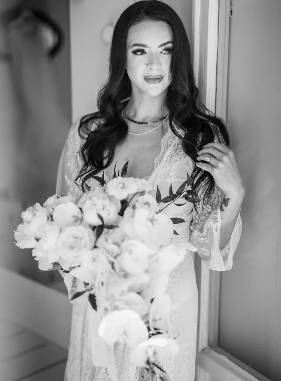 Ritratto in bianco e nero della sposa in vestaglia di pizzo con bouquet di peonie e orchidee
