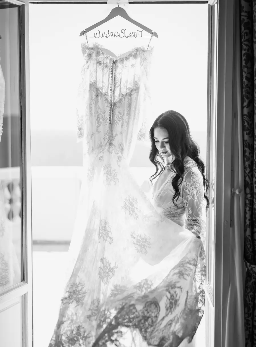 La sposa sfiora la gonna in pizzo dell'abito da sposa appeso, in bianco e nero