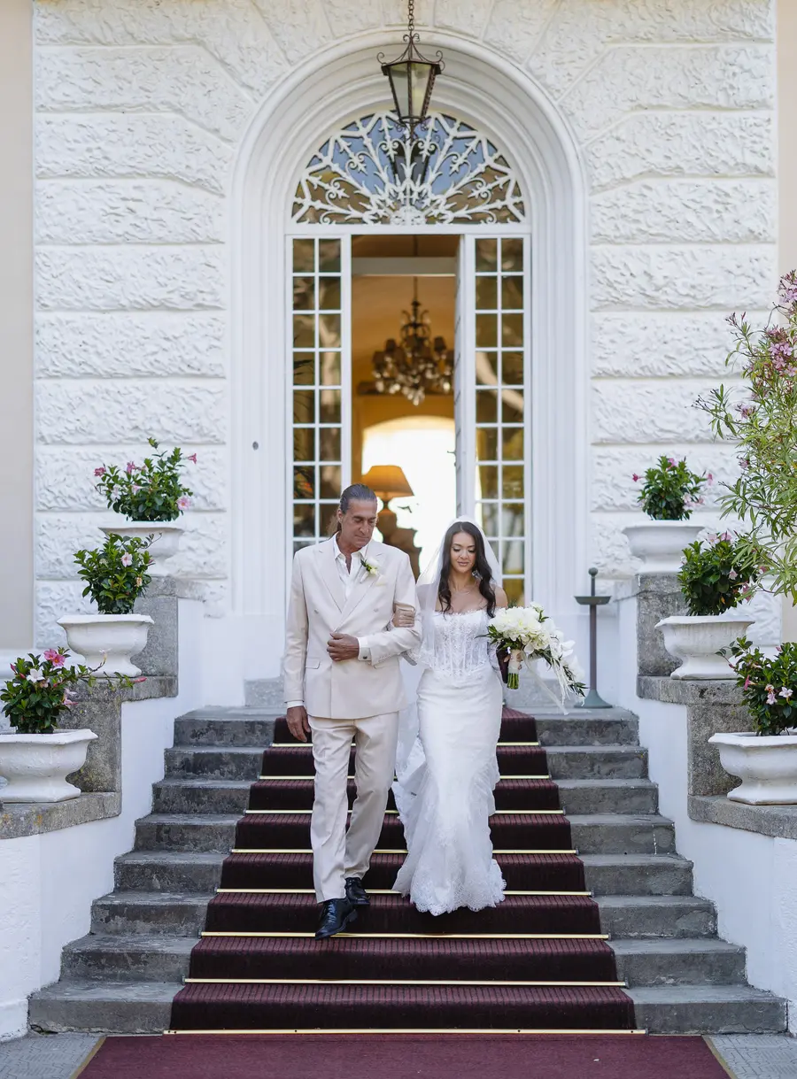 La sposa scende la scalinata di Villa Parisi a braccetto del padre sul tappeto rosso