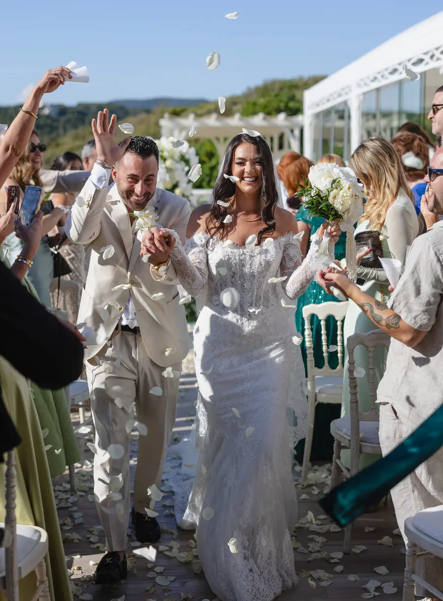 Gli sposi sorridenti escono dalla cerimonia tra i petali lanciati dagli invitati