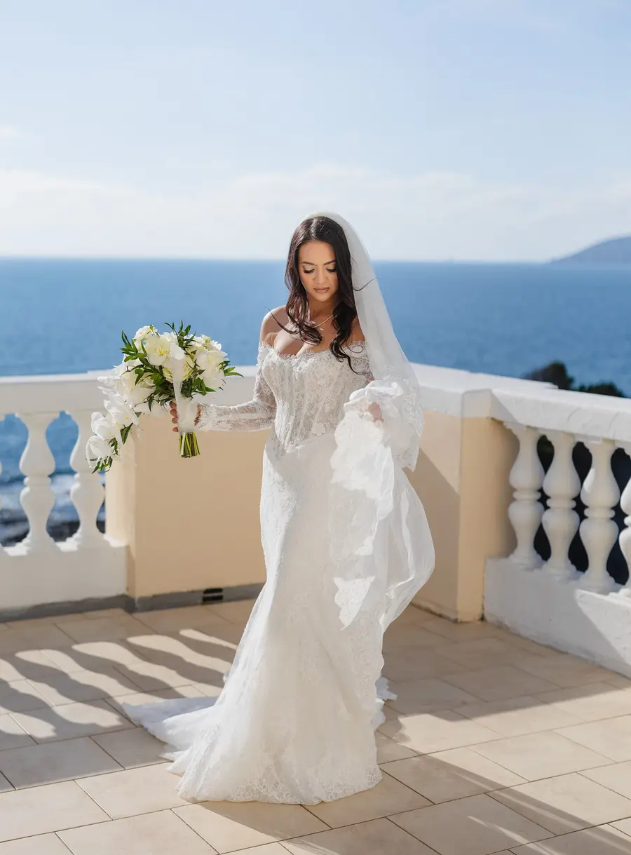 La sposa con abito in pizzo e bouquet cammina sulla terrazza a picco sul mare