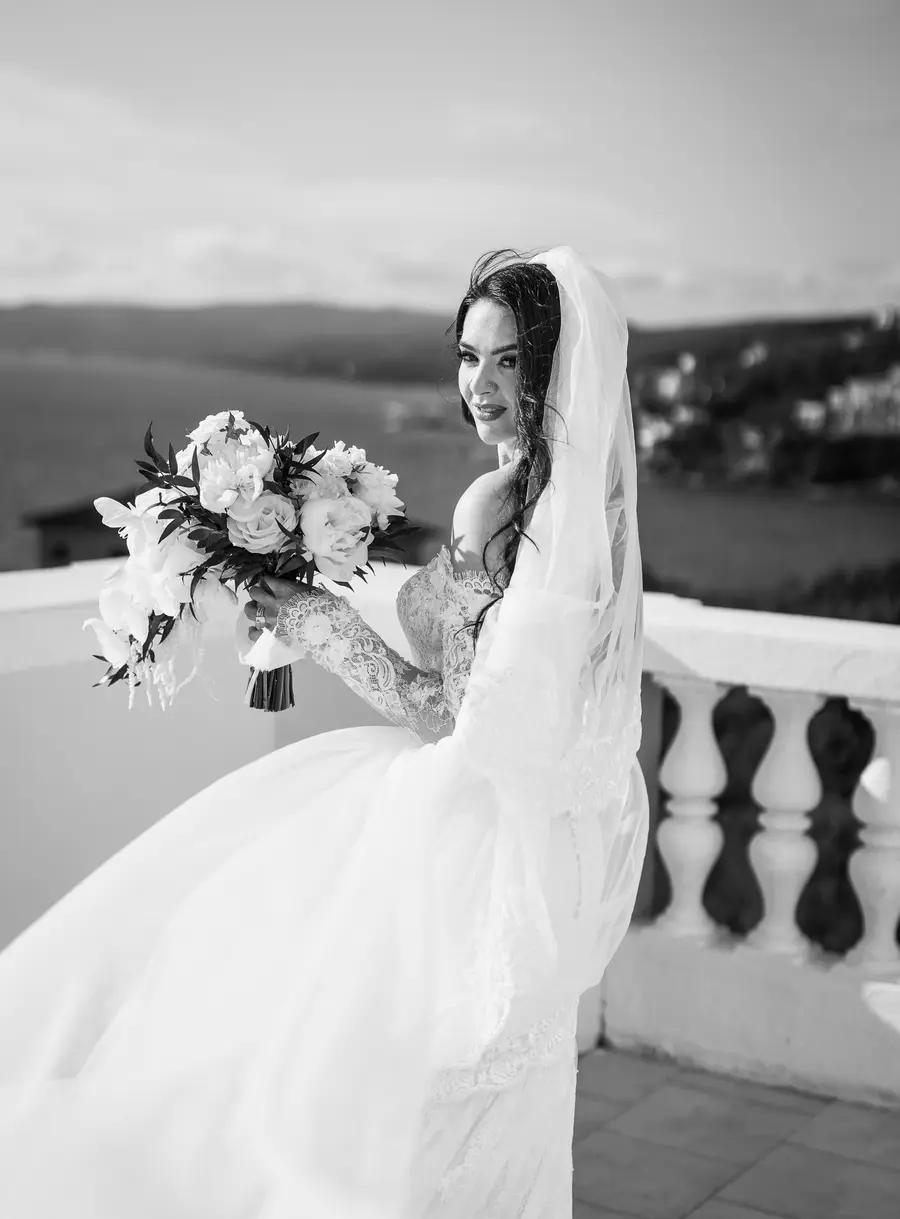 Sposa con velo mosso dal vento e bouquet vicino alla balaustra, ritratto in bianco e nero
