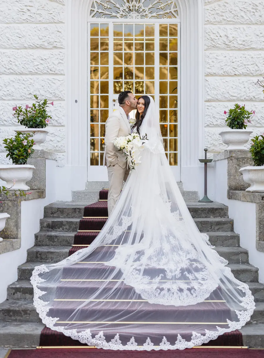Bacio sulla guancia sulla scalinata di Villa Parisi con il velo di pizzo a strascico