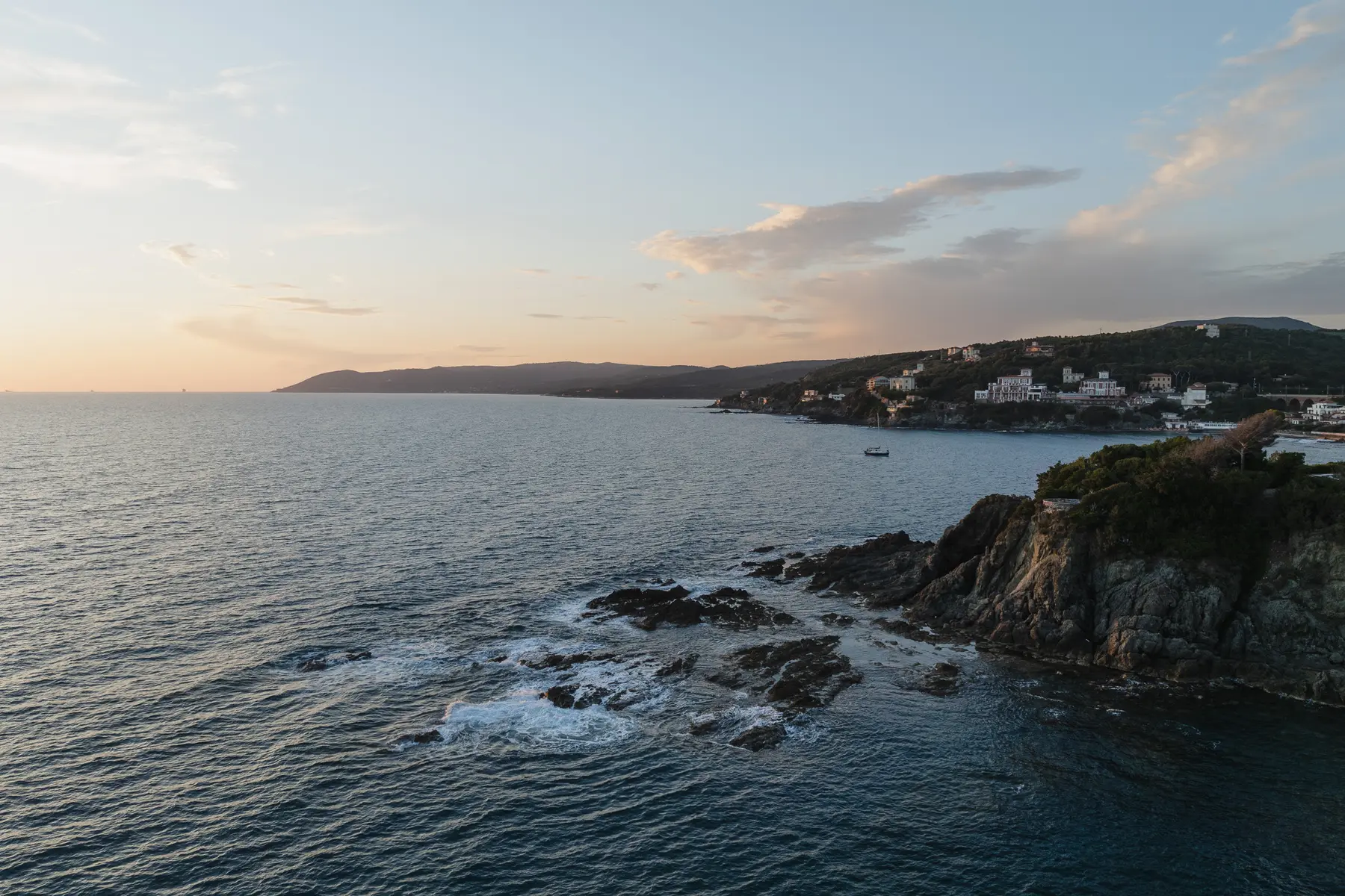 Veduta dall'alto della costa di Castiglioncello al tramonto con scogli e case sul promontorio