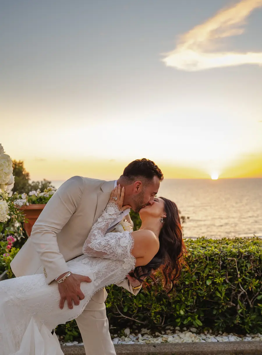 Bacio in casque degli sposi sulla terrazza con il sole che tramonta sul mare toscano