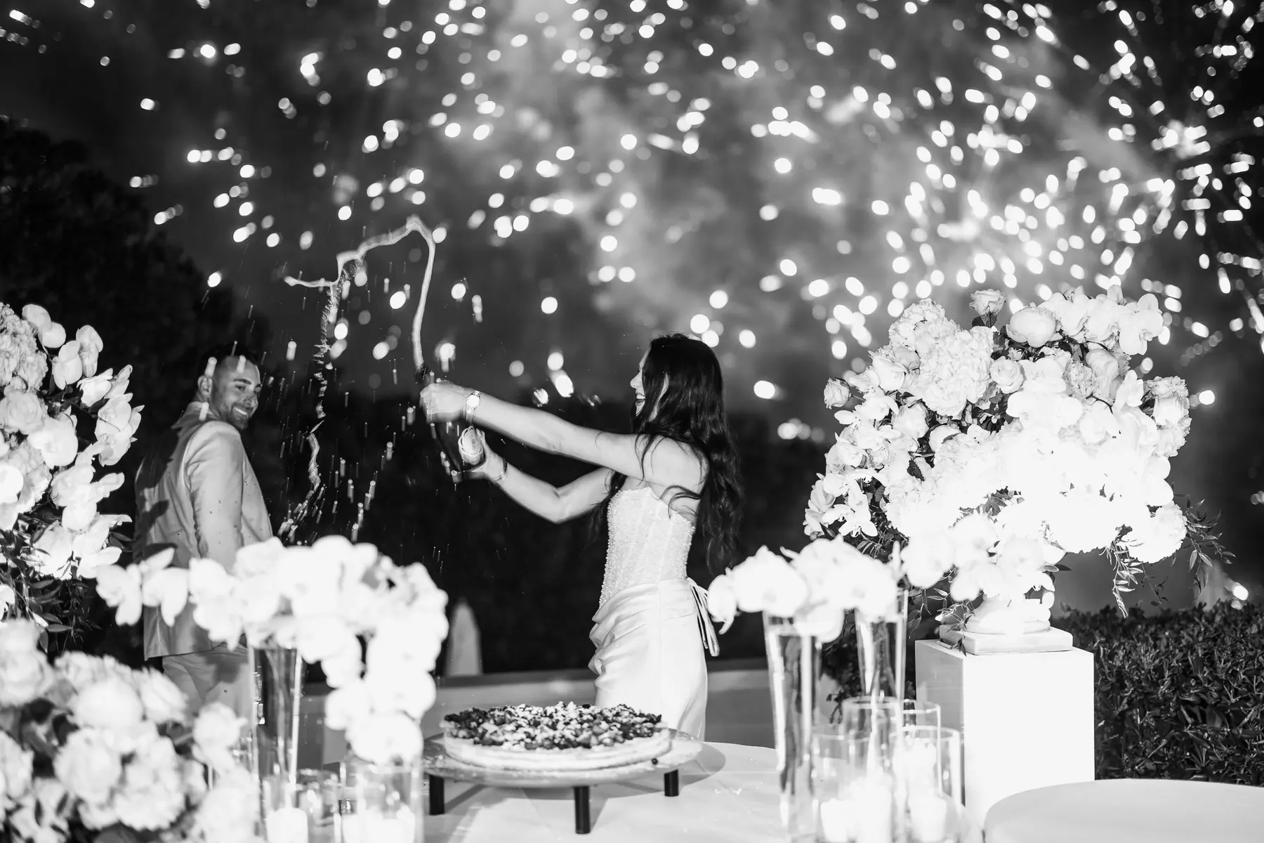 La sposa stappa lo spumante tra i fuochi d'artificio accanto alla torta, bianco e nero