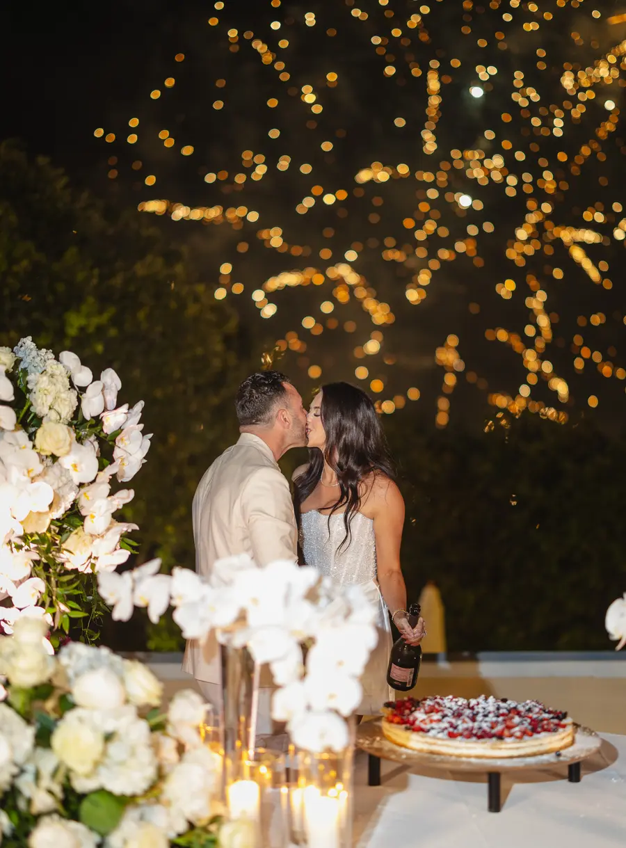 Gli sposi si baciano accanto alla torta ai frutti rossi con i fuochi d'artificio dorati